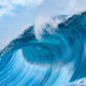 A wave crashes off Teahupoo, Tahiti, a popular surf break. The water is a rich turquoise blue and spray shoots off the top of the wave..